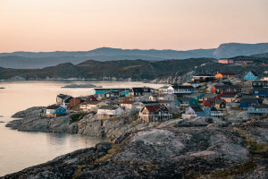 Aerial View of Arctic city of Ilulissat, Greenland during sunrise sunset. Colorful houses in the center of the town with icebergs in the background in summer on a sunny day with orange pink sky